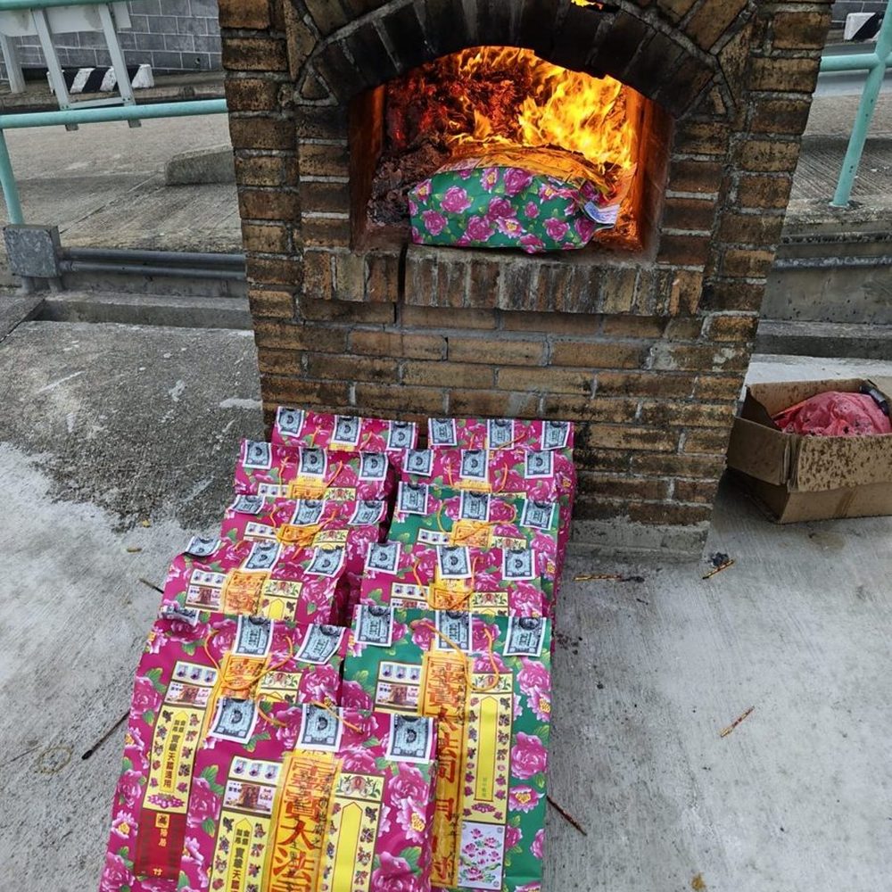 磚砌化寶爐前面地下鋪住一批寫好嘅衣包,爐口入面有火;袋面手寫嘅字已經打格仔遮住