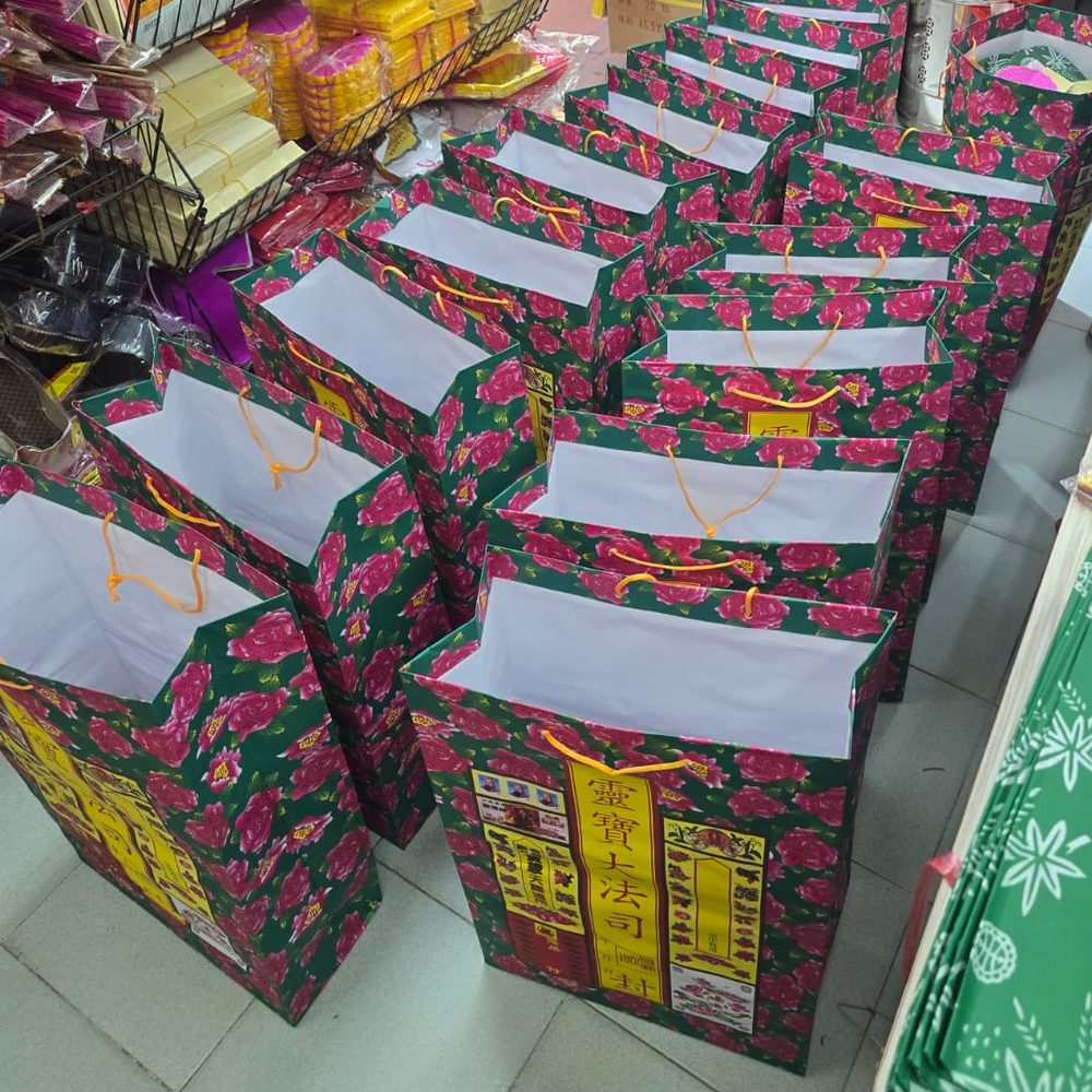一排排綠底玫瑰花紙嘅空衣包袋排喺地下,袋口打開、繫住橙色繩,等執料
